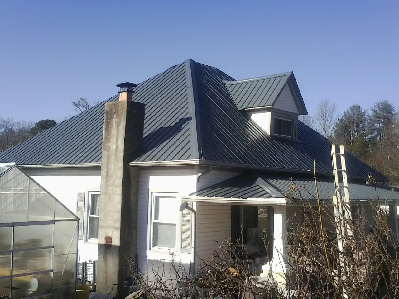 Dark blue standing seam metal roof on a white farmhouse with dormer — Slate & Tile Roof Repair by Roofing Brothers in Osteen