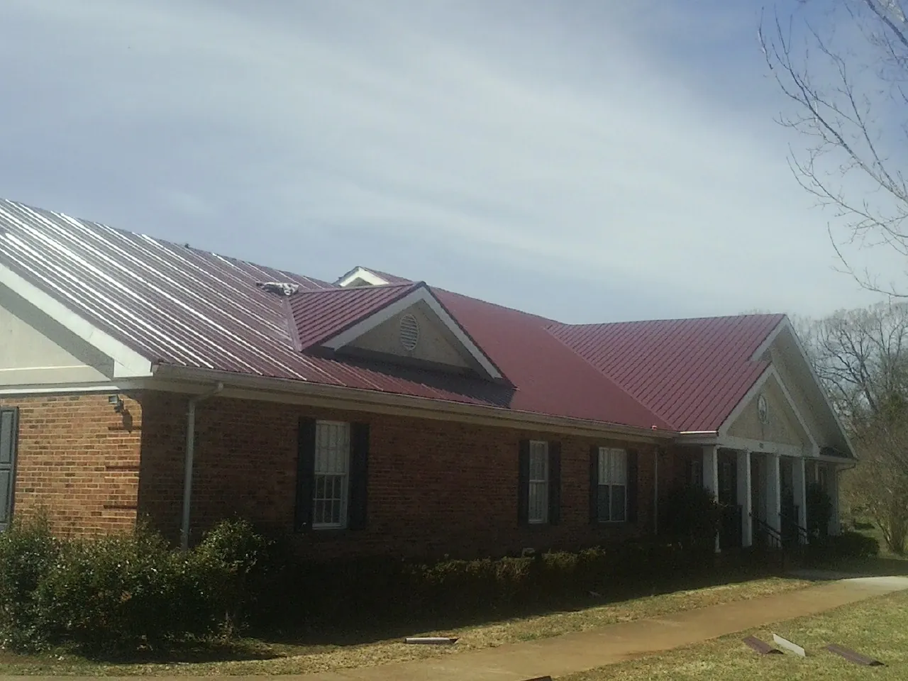 Red metal roof with gabled entries on a long brick building, from a Hail Damage Roof Repair job in Osteen