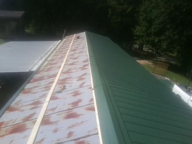 Old rusted panels beside newly installed green metal roofing — Wind Damage Roof Repair by Roofing Brothers in Osteen