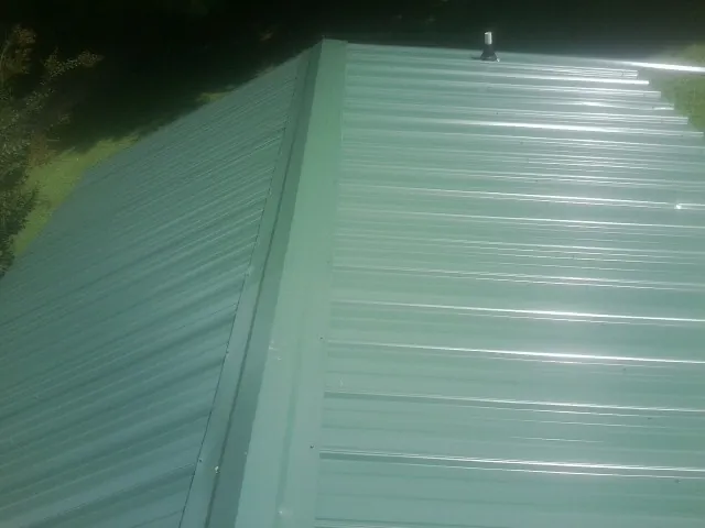 New green metal panels meeting at the ridge of a roof — Flat Roof Repair work by our crew in Osteen