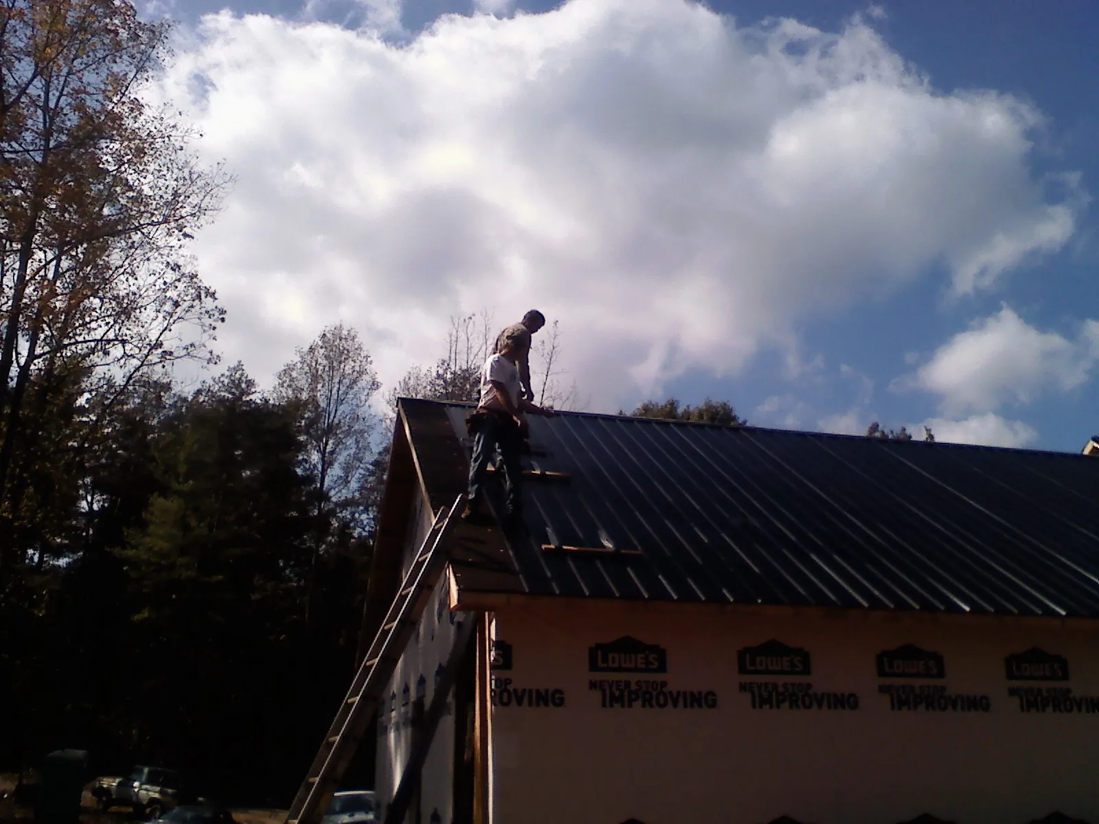 Roofer fastening dark metal panels high against a cloudy sky, from a Roof Inspection job in Osteen