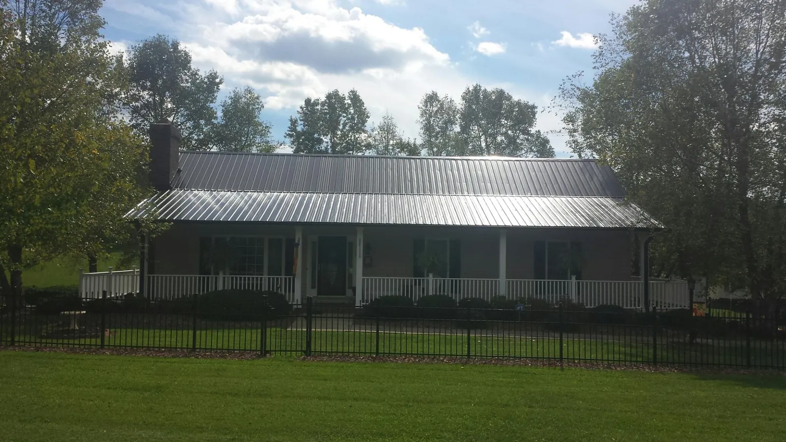 Gray metal roof on a brick ranch with a full width front porch — Gutter Guard Installation work by our crew in Osteen
