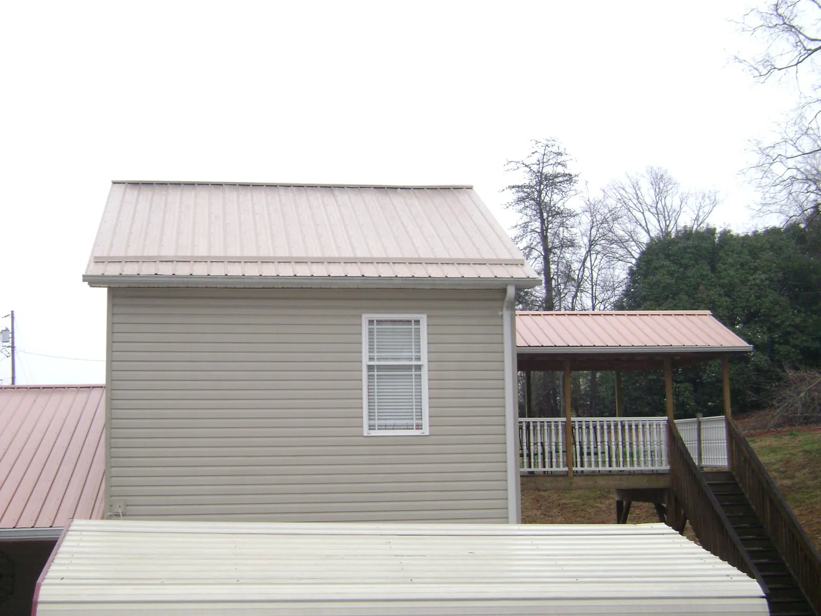 Tan metal roofs on a two story addition and attached porch, from a Roof Replacement job in Osteen